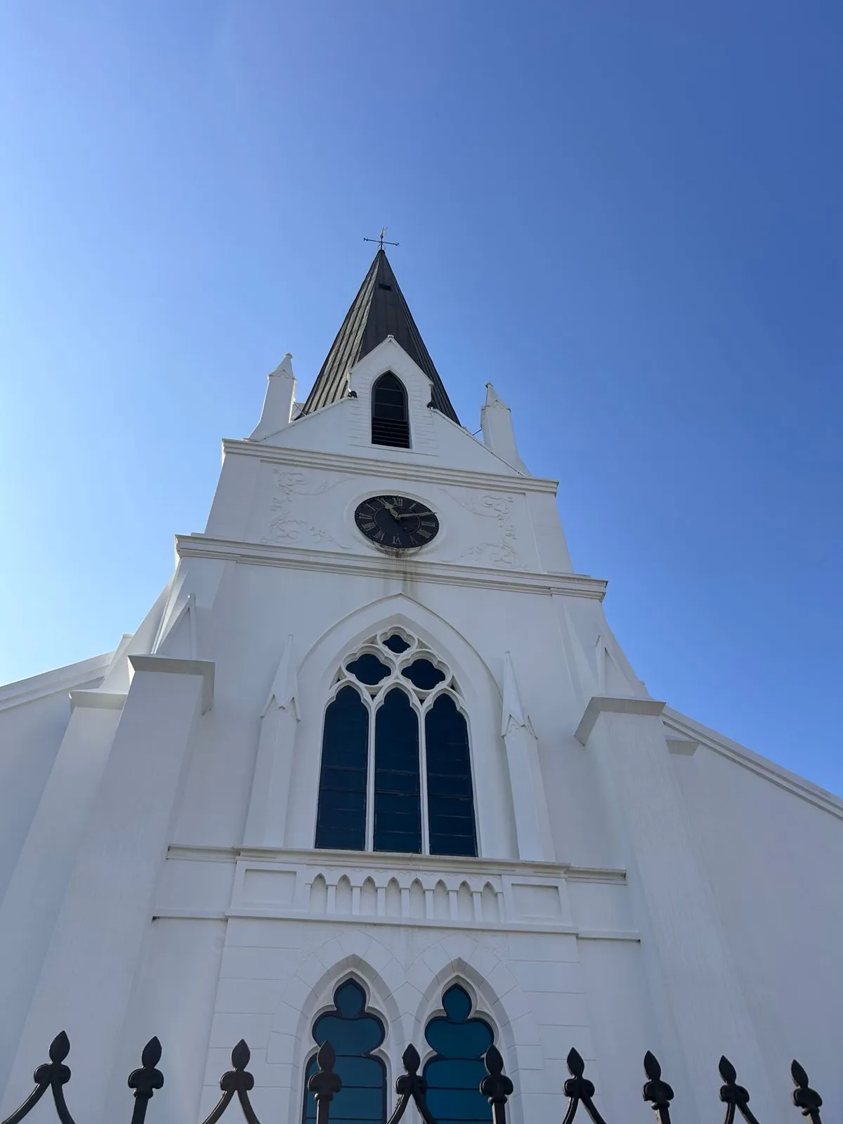 A historic white church with a tall steeple and clock rising against a clear blue winelands sky
